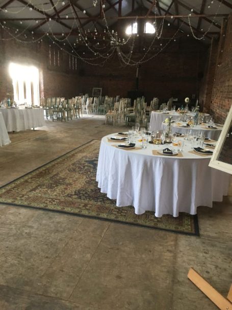 Tables set for a dining event in a rustic hall with decorative chandeliers.