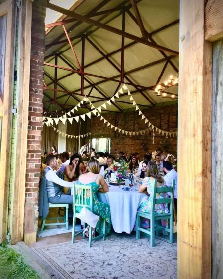 View of a dining area filled with guests, decorated with fairy lights and rustic furnishings.