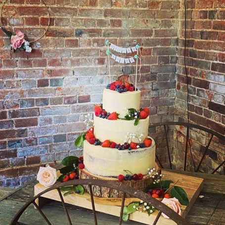 Three-tiered wedding cake adorned with fresh strawberries, blueberries, and decorative flowers.