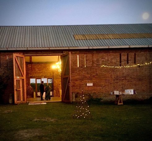 A rustic barn entrance with warm lights and a small decorative Christmas tree outside.